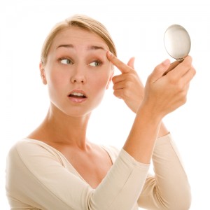 A young woman pulling up in her eyelid looking into a compact mirror